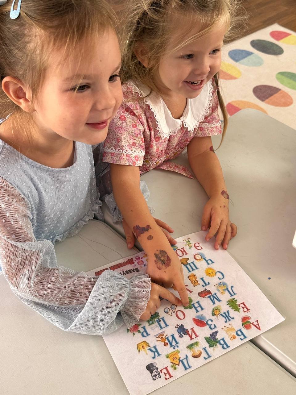 Two children exploring an illustrated alphabet chart together at Little Birds LA